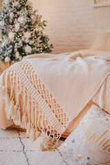 Fototapeta na wymiar Knitted light blanket with tassels on the bed in a cozy bedroom. Christmas interior in a Scandinavian style.