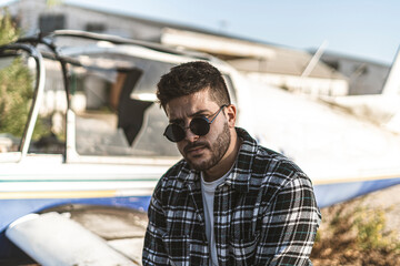 Hombre Joven adolescente modelo en una avioneta abandonada con camiseta y camisa de cuadros azules. 