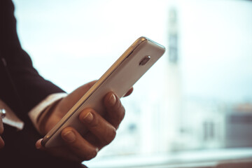 Businessman use smartphone for reading news in mobile seem alone relaxing near bangkok tower building window view at modern office in sunny day, Social media for using smart phone concept