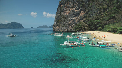 Philippines boat cruise aerial view. Tourists on passenger ships at sand shore. Local vessel tour of Palawan Island for travelers. Epic tropical Asia seascape of jungle mountain isle in cinematic shot