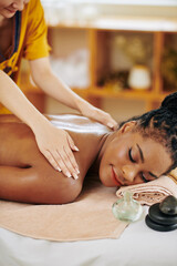 Cropped image of young Black woman enjoying back massage with oils in spa salon
