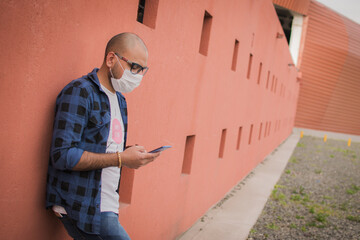 young latin man with protective mask using a cell phone, checking social networks outdoors