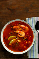 Tom yam soup with shrimp and lime in a light plate next to a spoon on a napkin.