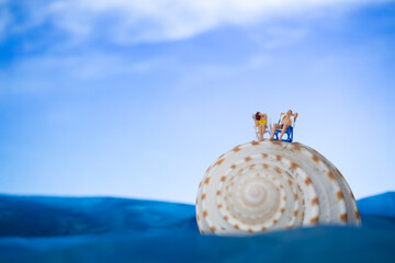 Fototapeta na wymiar Miniature people sunbathing on a seashell with blue sky background , summer vacation concept