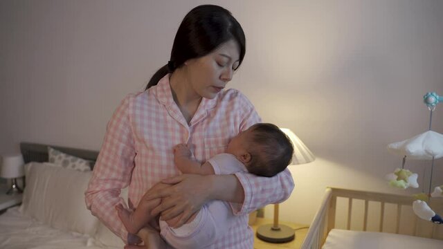 taiwanese female standing by crib is trying to hold properly while consoling by patting and touching softly on her baby daughter at home.