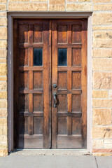 Antique western style wooden double doors on an old limestone block wall building in bright sunlight with copy space
