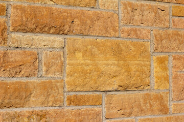 Full frame texture background of a vintage tan color exterior limestone block wall with bright sunlight and copy space