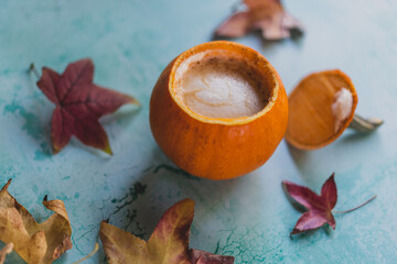 Fototapeta na wymiar pumpkin spice latte in pumpkin cup with fall leaves on turquoise background