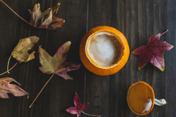 latte in pumpkin cup with autumn leaves on wood table