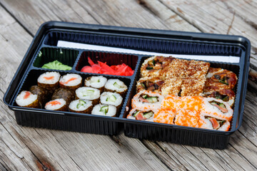 Set of sushi rolls in plastic box on wooden table. Sushi for take away or delivery of sushi in plastic container