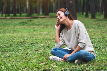 Naklejka na ściany i meble A beautiful young asian woman enjoy listening to music with headphone with feeling happy and relaxed in the park
