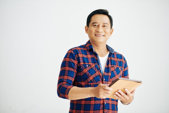 Portrait of smiling mature Asian man in plaid shirt holding tablet computer and looking at camera