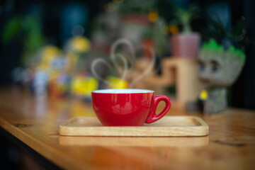 A red cup of coffee with shape love smoke on wood table in blurred Coffee Shop background.