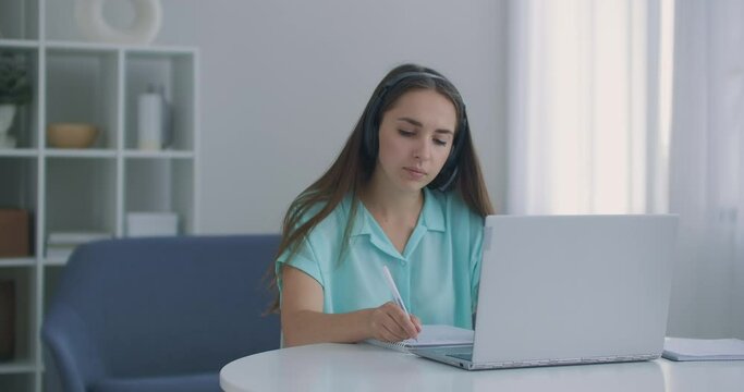 student woman sit at desk at home wear headset talk distantly by video call app and laptop device e-learn language studying with e tutor or classmate do common task remotely, modern tech concept