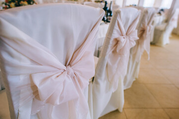 Row of beautiful chairs decorated with fabric and bows of delicate pink color in the wedding hall.