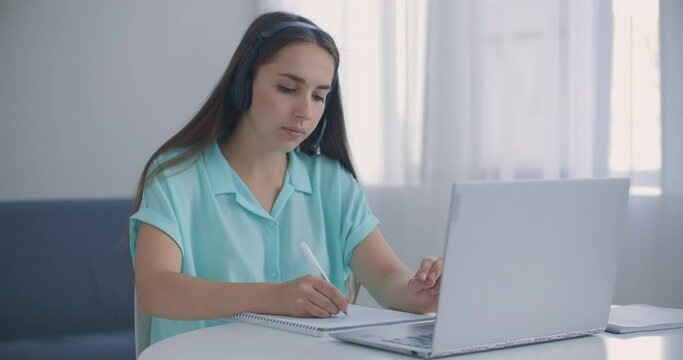 student woman sit at desk at home wear headset talk distantly by video call app and laptop device e-learn language studying with e tutor or classmate do common task remotely, modern tech concept