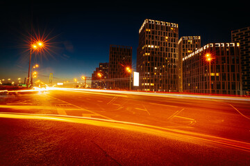 Fototapeta na wymiar City street at night. Light trails from moving cars on the dusk urban road with modern buildings on the opposite side.