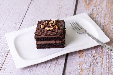 chocolate cakes pastries brownies on white ceramic plate with nuts topping  on a white wooden...