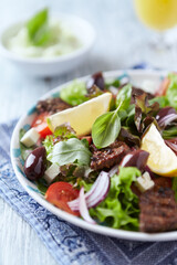 Tasty Salad with Grilled Beef Pieces, Cherry Tomatoes, feta Cheese and Kalamata Olives. Bright wooden background. Close up.	