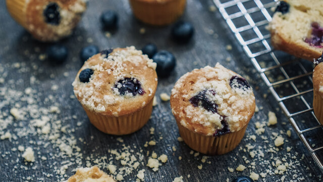 Blueberry muffin topped with crumble on a dark textured background and cooling rack