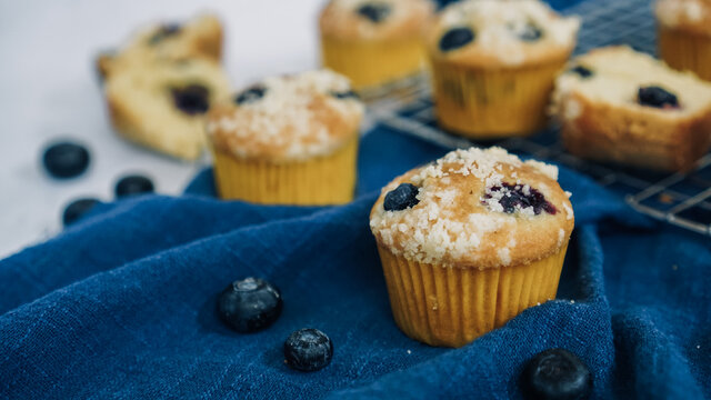 Crumbled Blueberry muffin on a blue cloth and white marble background