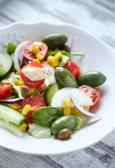 Healthy Salad with Green Olives, Baby Spinach, Cucumber, Cherry Tomatoes and Capers. Bright wooden background. Close up.	