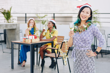 Pretty young Chinese woman in Santa hat celebrating Christmas with her friends in cafe on rooftop