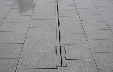 large-format paving made of gray granite. the water is drained in the rain through a slotted stainless steel channel which is sunk under the surface of the tile.