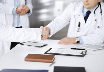 Unknown doctors are shaking their hands as agreement about patient's diagnosis, close-up. Medical help, insurance in health care, medicine concept