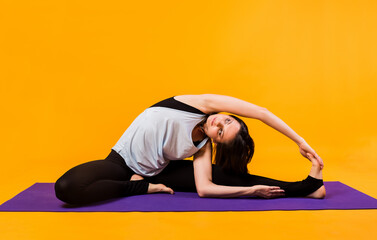 Fototapeta na wymiar a woman in a tracksuit performs stretching on a purple Mat on an orange background