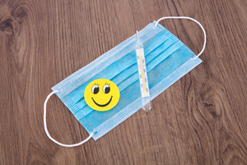 Thermometer and smiley pendant on blue disposable mask