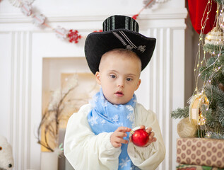 A boy with Down syndrome decorates a Christmas tree with balls, a child with a disability in a...
