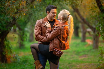 The happy couple, man and woman posing outdoor in the green autumn park in the red bomber leather...