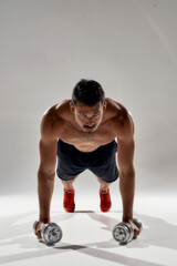 Working out. Young strong athletic man doing push ups on weights isolated over grey background