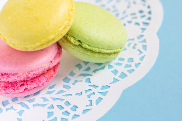 Close up view of multicolored almond french macarons on white ornated napkin on blue background. French traditional pastry