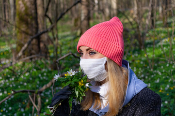 Girl in a mask in the forest with a bouquet of flowers.