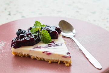 Piece of blueberry cheesecake on ceramic plate with peppermint leaves on top.