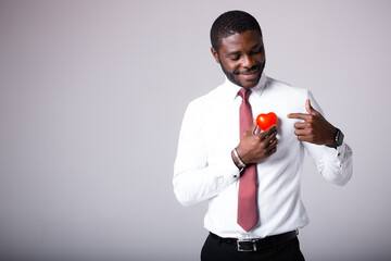 A male African American cardiologist stands in a white shirt with a red heart in his hands. Space...