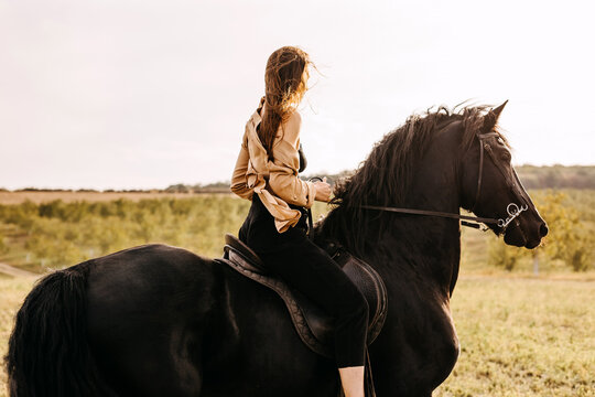 Young woman riding a black friesian horse, outdoors.