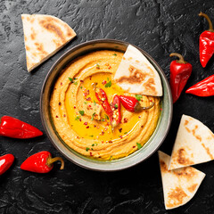 Roasted red pepper hummus with pita bread on black background. top view