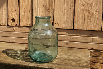 Empty glass jar. A three liter jar stands on a wooden bench near the house.