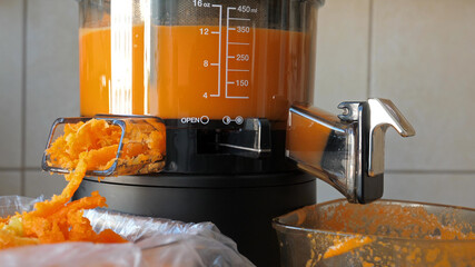 Slow juicer is making fresh carrot and orange juice.