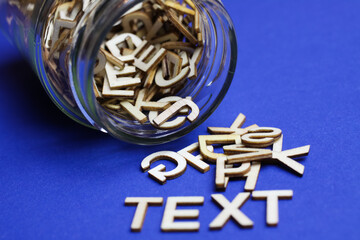 Close up of tipped over glass jar with chaotic scattered alphabet letters on blue background forming the word text
