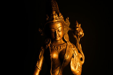 Fototapeta na wymiar Close up of isolated illuminated hindu Shiva god golden bronze statue with raised hand on blank black background