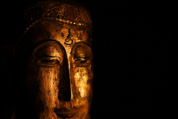 Fototapeta na wymiar Closeup of isolated illuminated golden Buddha face mask on black blank background with copy space for text