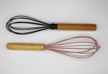 Top down view on isolated whisks with wood handle, pink and black wire loops on blank white...