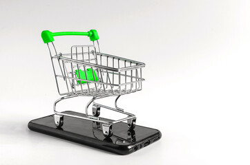 green from the supermarket trolley standing on a smartphone on a light background, the concept of online trading