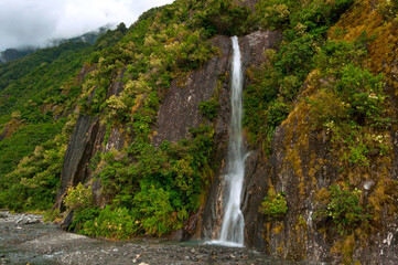 Waterfall among rocks and green plants near Franz Josef Glacier, South Island, New Zealand