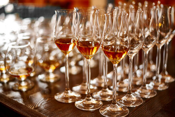 Glasses with brandy or cognac stand in a row. Blurred background, warm tinted. Tasting glasses with aged french cognac brandy