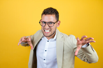 Young handsome businessman wearing suit over isolated yellow background smiling funny doing claw...